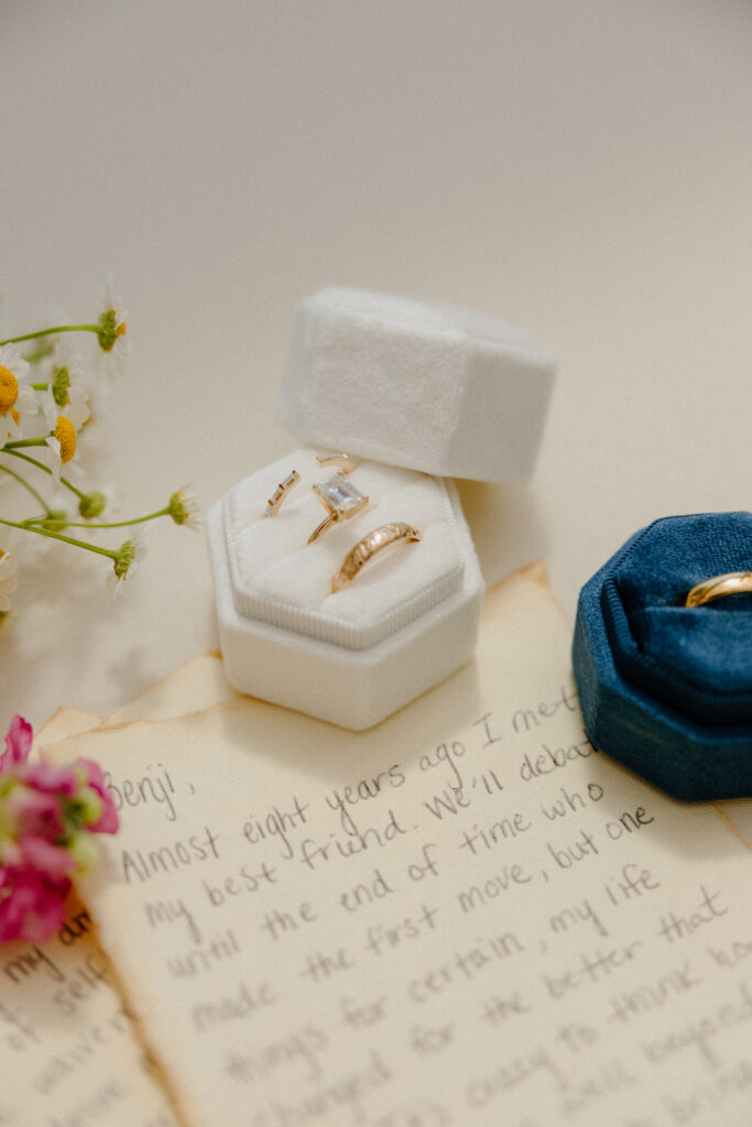 wedding rings in white and blue velvet boxes sitting on top of wedding vows.